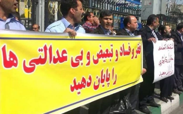 A group of people hold a gathering and raise a banner reading "End the poverty, corruption, discrimination, and injustice."
